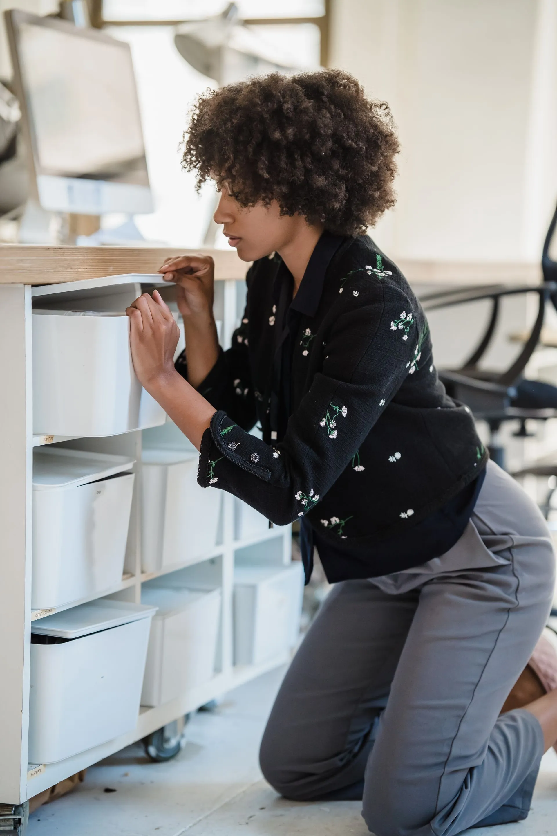 A woman kneeling to search through a filing cabinet in an office
