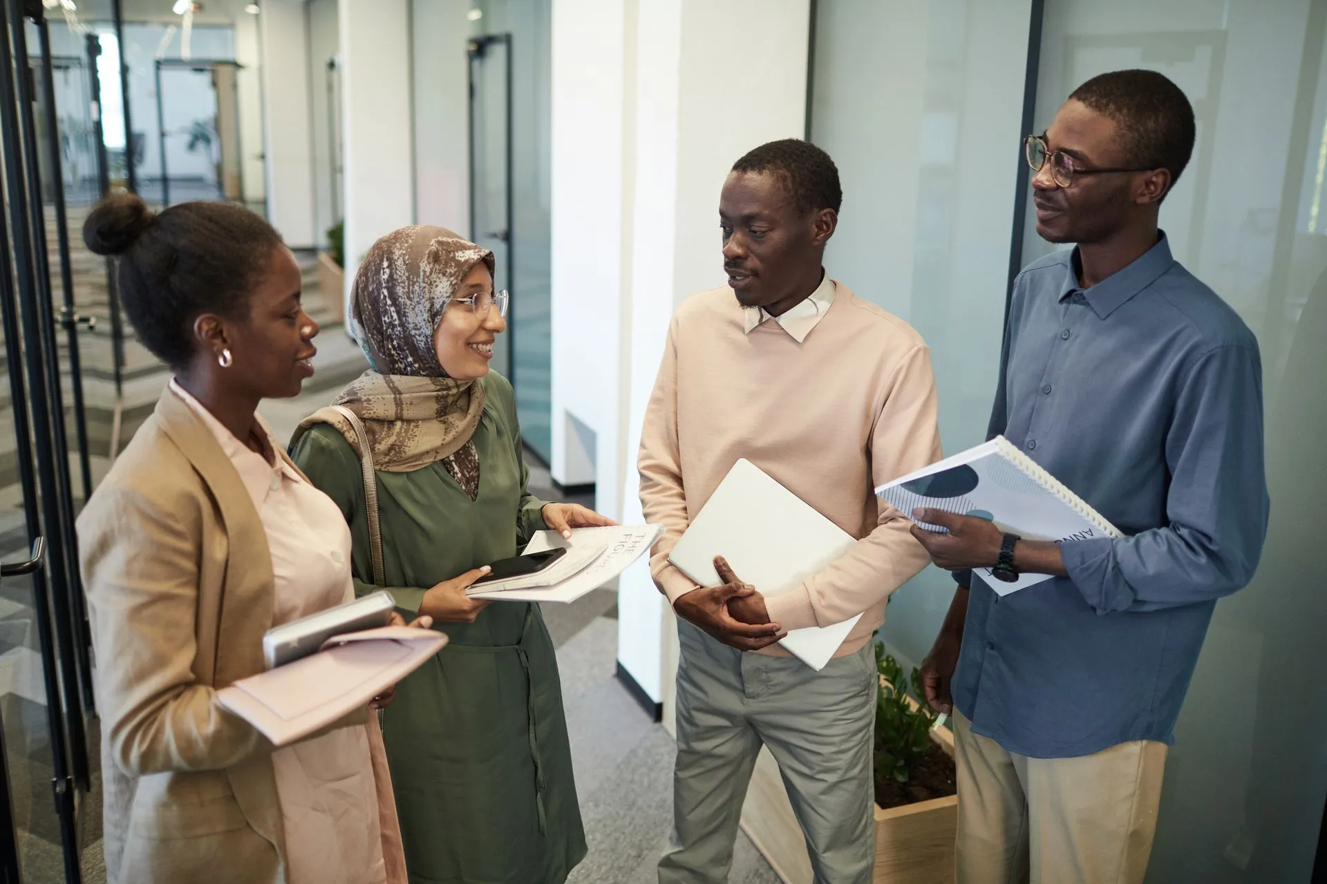 A small group of colleagues, including a woman wearing a hijab, discussing a document together in an office